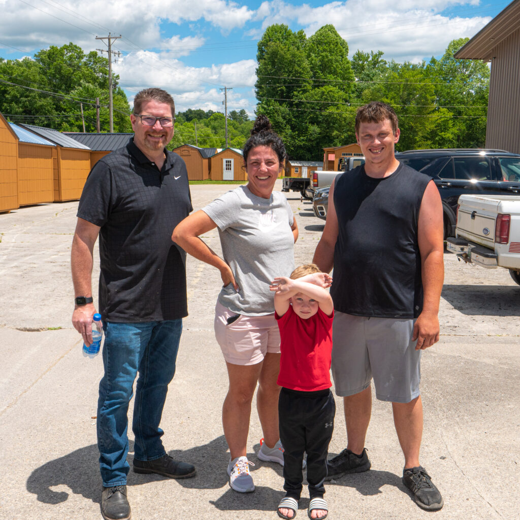 A Picture of Walteena Hollis with her brother-in-law Eric, her son Havlin, and Grandson standing in front of Shedmax.